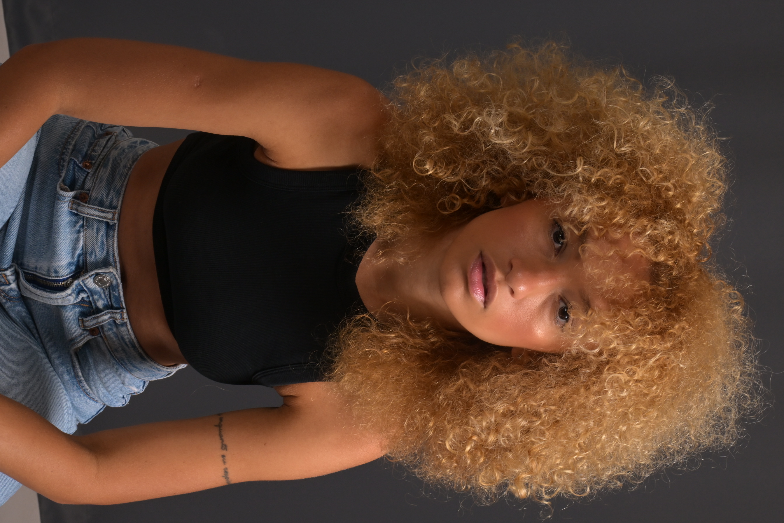 Front portrait of Nalu in a black top and jeans against a dark background.